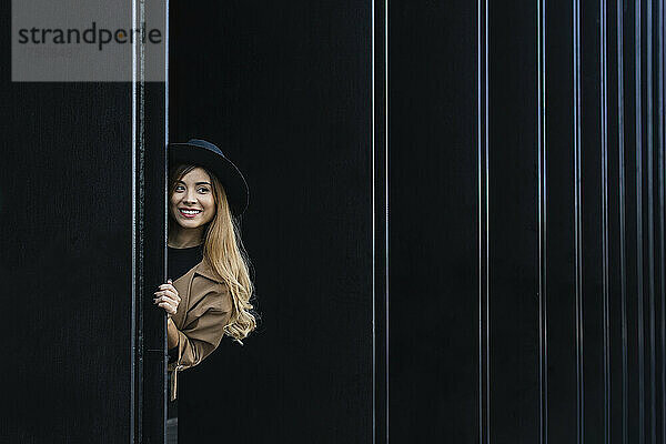 Frau mit Hut lächelt hinter der Wand