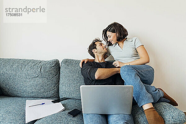 Lächelndes junges Paar  das einander anschaut  während es zu Hause arbeitet