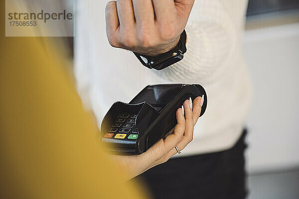 Mann bezahlt per Smartwatch an Kellnerin mit Kreditkartenlesegerät im Café