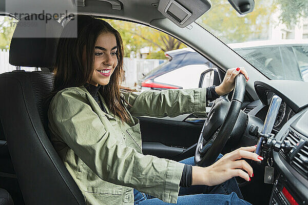 Lächelnde junge Frau benutzt Mobiltelefon im Auto