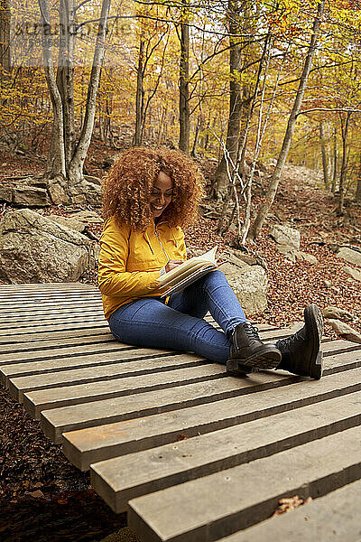 Lächelnde junge Frau liest Buch im Herbstwald