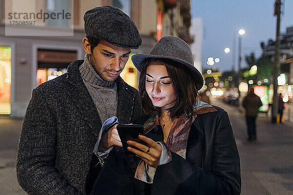 Freundin und Freund nutzen gemeinsam Mobiltelefon in der Stadt