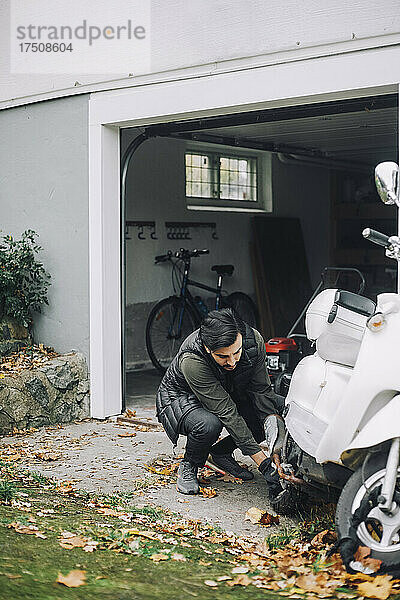 Mittlerer Erwachsener  der einen Motorroller in einer Garage im Hinterhof repariert