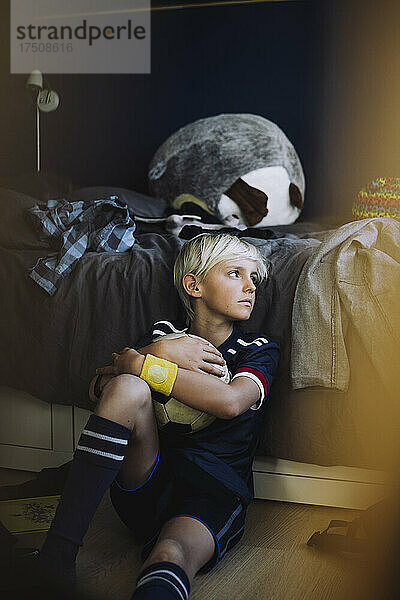 Trauriger Junge mit Fußball  der im Schlafzimmer wegschaut