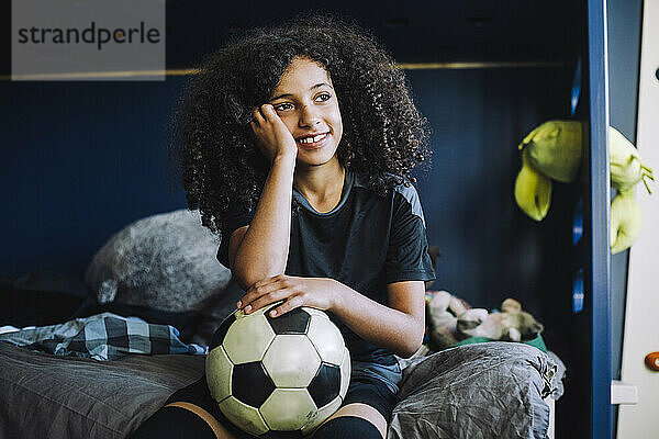 Nachdenkliches Mädchen mit Fußball im Schlafzimmer