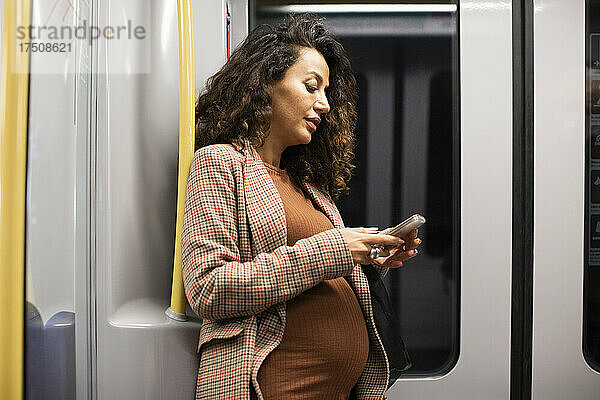 Schwangere Unternehmerin bei der Nutzung eines Smartphones während einer Zugfahrt