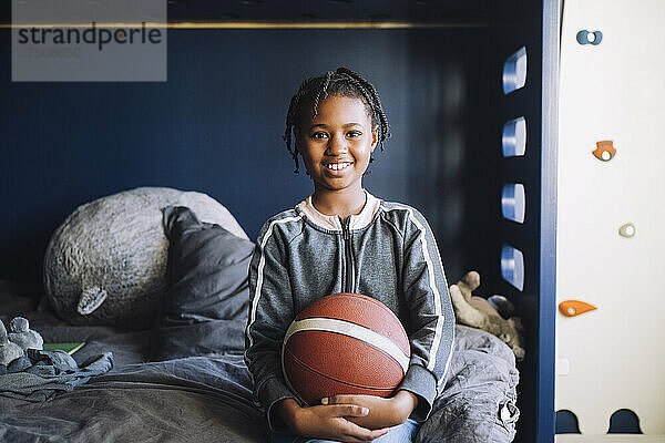 Porträt eines lächelnden Mädchens mit Basketball  das im Schlafzimmer sitzt