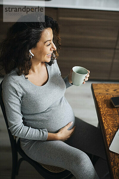 Schwangere Freiberuflerin im Gespräch über Bluetooth bei einem Kaffee zu Hause