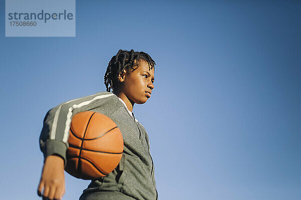 Mädchen schaut weg mit Basketball durch klaren Himmel