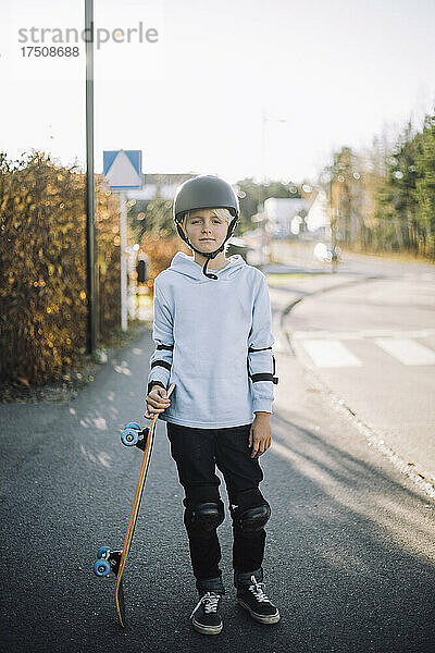 Porträt eines Jungen mit weißem Skateboard auf der Straße stehend