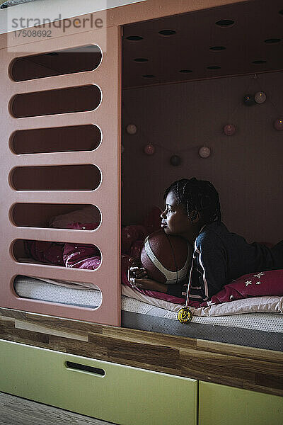 Mädchen liegt mit Basketball auf dem Bett im Schlafzimmer