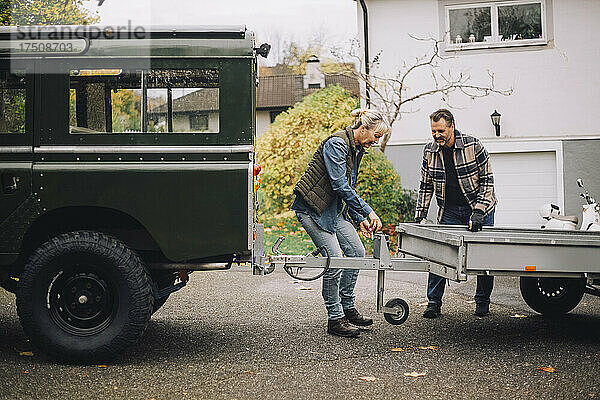 Älteres Paar  das einen Anhänger an einen Geländewagen in der Einfahrt zieht