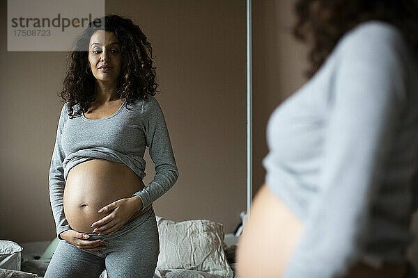Schwangere Frau schaut in den Spiegel zu Hause