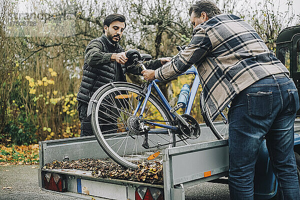 Sohn und Vater laden Fahrrad in Fahrzeuganhänger auf Einfahrt