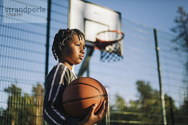 Kontemplatives Mädchen  das an einem sonnigen Tag mit einem Basketball wegschaut