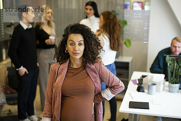 Porträt einer schwangeren Geschäftsfrau mit Kollegen im Hintergrund im Büro