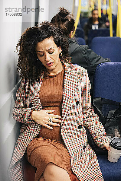 Schwangere Geschäftsfrau berührt Bauch beim Sitzen im Zug