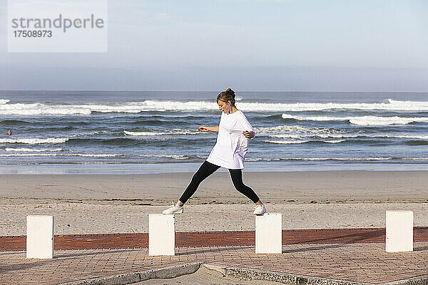 Ein Mädchen im Teenageralter balanciert auf Pfählen an einem Sandstrand.