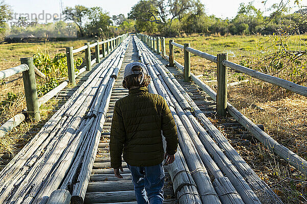 Ein Junge  der allein über eine Holzbrücke im Sumpfgebiet geht