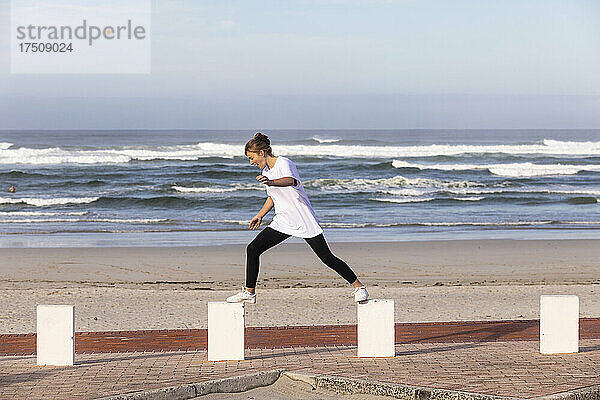Ein Mädchen im Teenageralter balanciert auf Pfählen an einem Sandstrand.