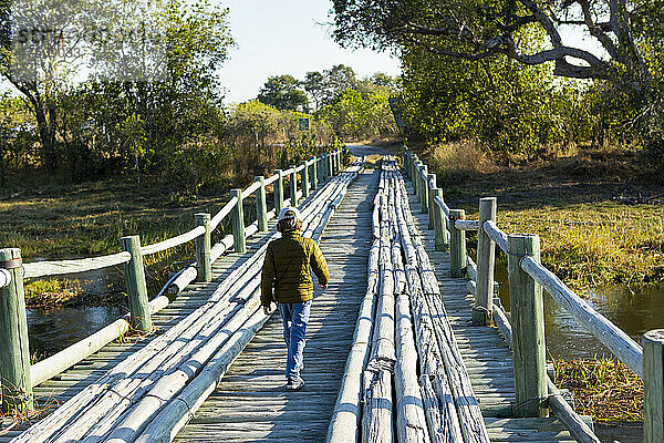 Ein Junge  der allein über eine Holzbrücke im Sumpfgebiet geht