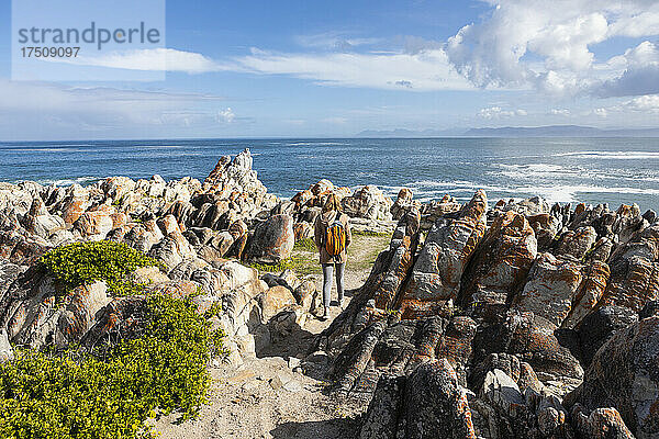 Teenager-Mädchen mit Rucksack auf den Felsen stehend mit Blick auf den Ozean