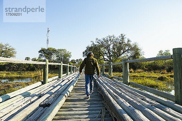 Ein Junge  der allein über eine Holzbrücke im Sumpfgebiet geht