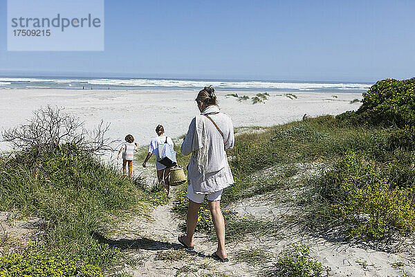 Eine Familie  die mit Körben und Taschen durch die Sanddünen in Richtung Meer läuft.