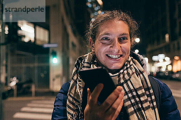 Italien  lächelnder Mann mit Smartphone in der Nacht in der Stadt