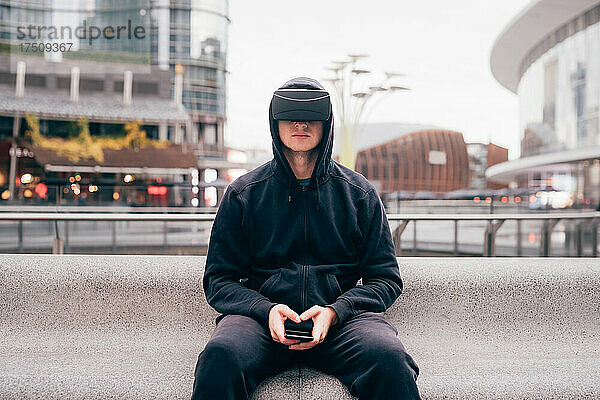 Italien  Mann mit VR-Brille sitzt auf Mauer in der Stadt