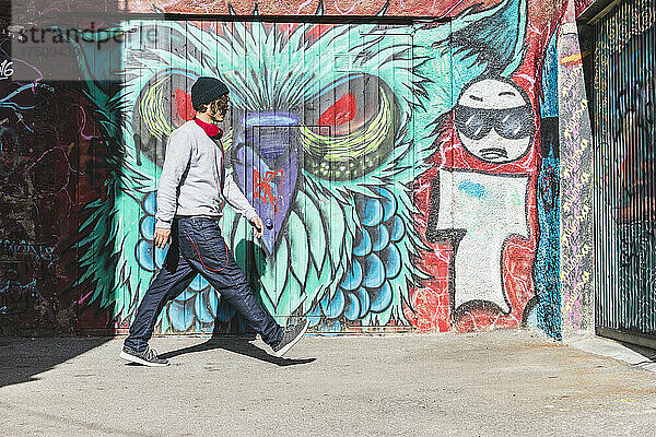 Junger Mann mit Kopfhörern läuft vor Graffiti