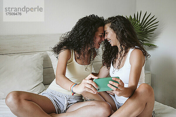 Fröhliches lesbisches Paar macht ein Selfie mit dem Smartphone  während es zu Hause im Bett sitzt