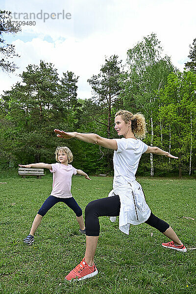 Mutter und Tochter üben Krieger-2-Pose auf Grasland im Wald