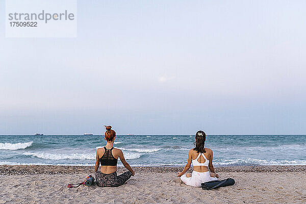 Junge Frauen meditieren am Strand bei klarem Himmel bei Sonnenuntergang