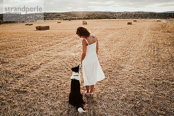 Frau steht bei Sonnenuntergang neben Hund im Feld