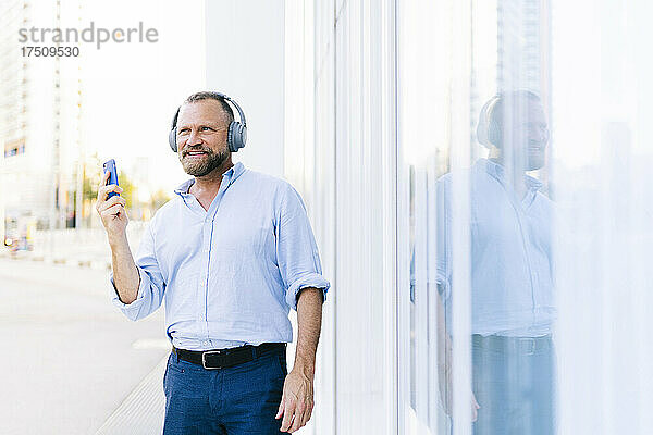 Geschäftsmann hält Smartphone in der Hand  während er in der Stadt Musik hört