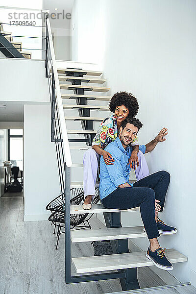 Glückliches Paar sitzt auf schwebender Treppe in modernem Penthouse