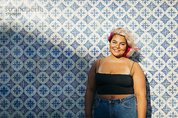 Lächelnde junge Frau  die vor einer gemusterten Wand steht