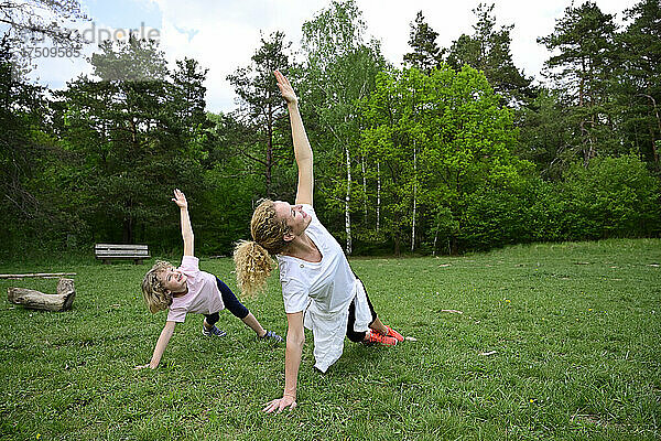 Mutter und Tochter üben Sideplank-Pose auf Grasfläche im Wald