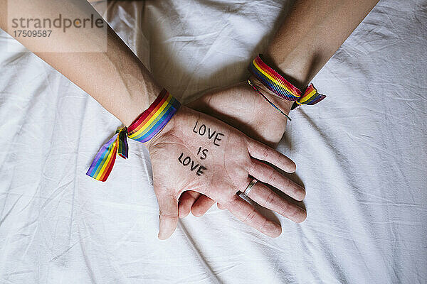 Nahaufnahme der Hände eines lesbischen Paares mit Text auf dem Bett zu Hause