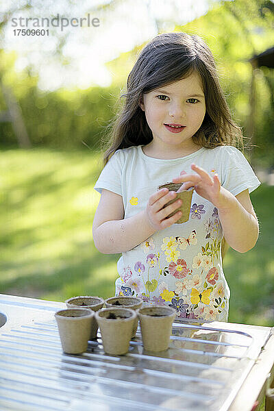 Nettes Mädchen pflanzt Samen in kleinen Töpfen auf dem Tisch im Garten