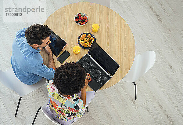 Glückliches Paar mit Laptop und digitalem Tablet am Esstisch im Penthouse