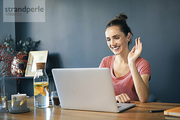 Lächelnde Unternehmerin führt Videokonferenzen über Laptop auf dem Schreibtisch im Heimbüro