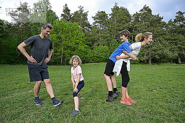 Glückliche Eltern trainieren mit Kindern auf Grasland gegen Bäume im Wald