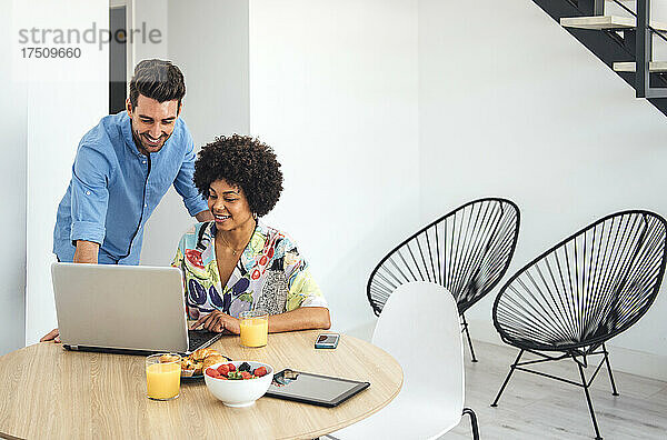 Glückliches Paar benutzt Laptop am Esstisch im modernen Penthouse