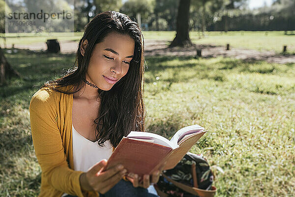 Junge Frau liest ein Buch  während sie auf einer Wiese im Park sitzt