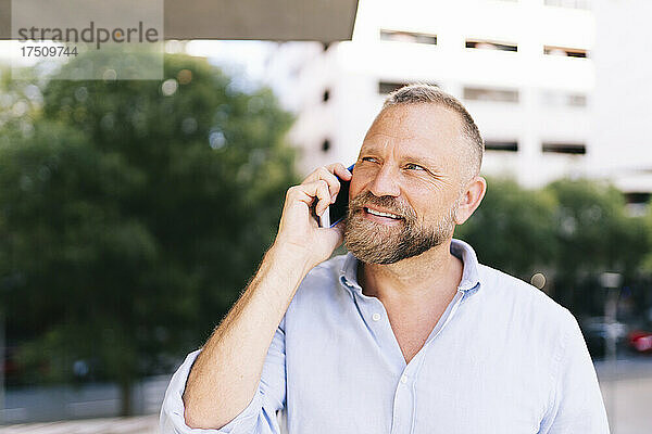 Nahaufnahme eines lächelnden männlichen Unternehmers  der mit dem Mobiltelefon spricht