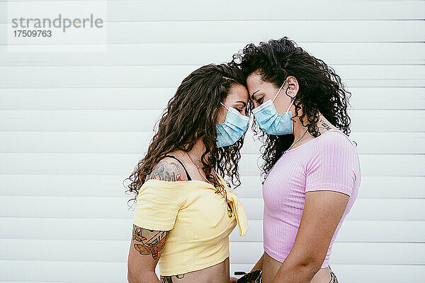 Lesbisches Paar mit Masken und Angesicht zu Angesicht steht in der Stadt an der Wand