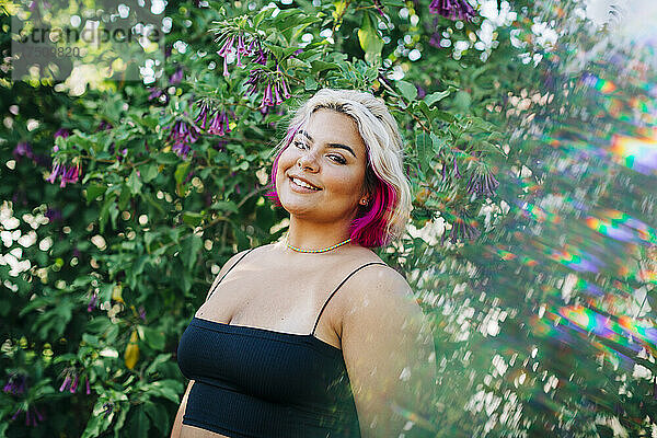 Lächelnde  kräftige Frau  die draußen neben einer blühenden Pflanze steht