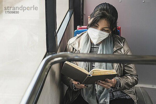 Frau trägt Schutzmaske  während sie im Bus ein Buch liest